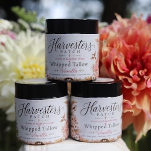 May include: Three cylindrical jars of Harvesters Patch Whipped Tallow Vanilla, each featuring a black lid and a white label with floral illustrations, black script text, and the product name clearly printed on the front of the containers.