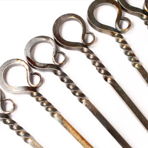 May include: Set of six metal skewers with twisted handles and a loop at the top. The skewers are a rustic silver color with brown rust spots.