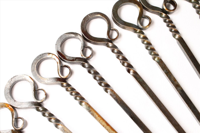 May include: Set of six metal skewers with twisted handles and a loop at the top. The skewers are a rustic silver color with brown rust spots.
