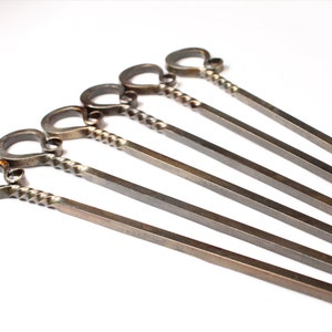 May include: Set of six silver metal skewers with a twisted handle and a loop at the end.