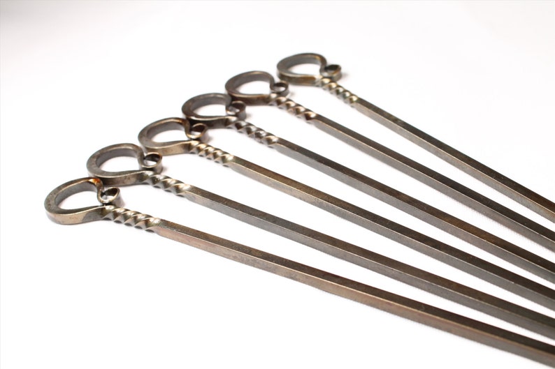 May include: Set of six silver metal skewers with a twisted handle and a loop at the end.