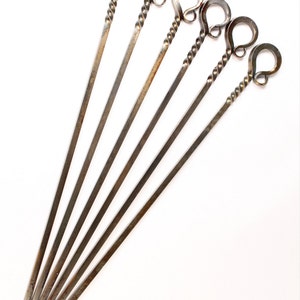May include: Set of six metal skewers with twisted handles. Each handle has a loop at the top.