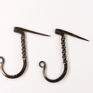 May include: Two antique-looking metal hooks with a twisted design. The hooks have a pointed end and a loop at the bottom.
