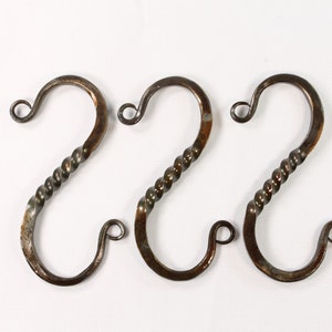 May include: Three rustic, hand-forged metal hooks with a twisted design. The hooks are approximately 3 inches long and have a dark brown finish.