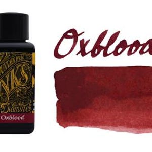 May include: A black bottle of Diamine fountain pen ink with a decorative gold and black label featuring the text Oxblood. Next to the bottle is a rectangular swatch of deep red ink, with the word Oxblood written in a matching red script font.
