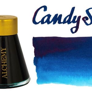 May include: A glass ink bottle with a gold cap and the word Alchemy printed in gold on the side. Next to the bottle is a handwritten text Candy Sea and a rectangular watercolor swatch that transitions from deep dark purple to bright cyan blue.