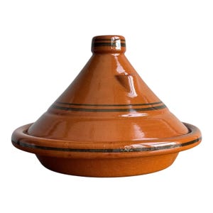 May include: A glazed terracotta tagine cooking vessel featuring a conical lid with a small knob handle. The exterior surface is a warm orange-brown color, accented by thin, dark brown horizontal stripes encircling the base and lid.