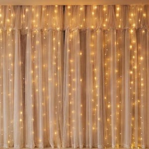 May include: Sheer white curtains featuring vertical strands of warm white LED fairy lights. The fabric is gathered at the top with a ruffled header, creating a soft, layered appearance with evenly spaced glowing light points throughout.