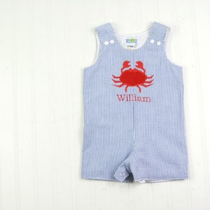 Könnte beinhalten: Blaue und weiße gestreifte Baby-Latzhosen mit einem roten gestickten Krebs und dem Namen "William" auf der Vorderseite.
