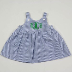 K&ouml;nnte beinhalten: Ein blaues und wei&szlig; gestreiftes Kleid mit einem gr&uuml;nen Monogramm auf der Vorderseite. Das Kleid ist &auml;rmellos und hat einen R&uuml;schenkragen.