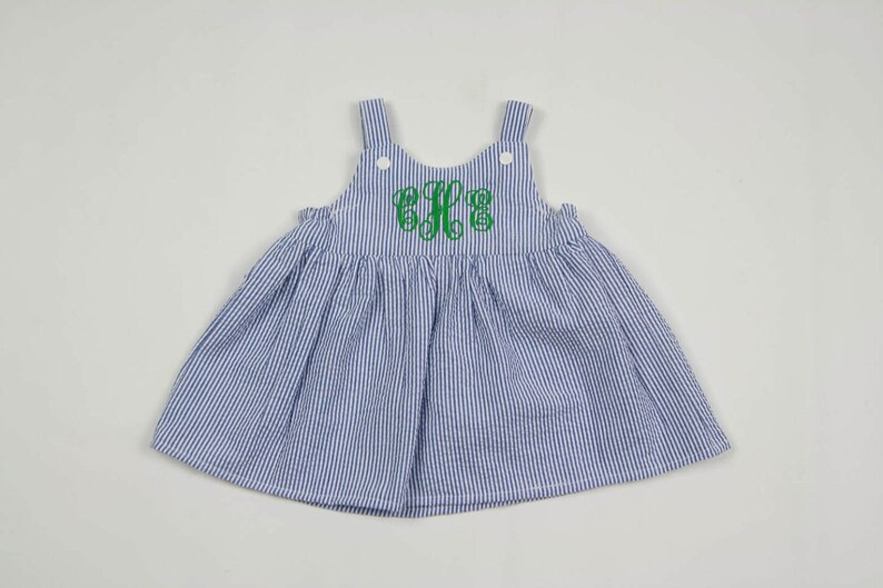 K&ouml;nnte beinhalten: Ein blaues und wei&szlig; gestreiftes Kleid mit einem gr&uuml;nen Monogramm auf der Vorderseite. Das Kleid ist &auml;rmellos und hat einen R&uuml;schenkragen.