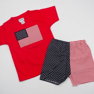 May include: Red short-sleeved t-shirt with a blue and red American flag design. Matching red, white, and blue patterned shorts.