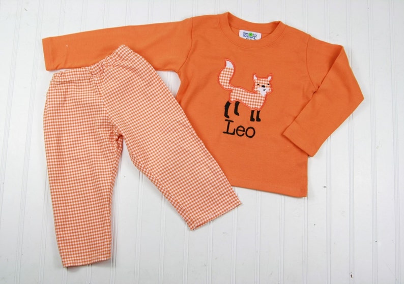 May include: Orange and white gingham pants and a long-sleeved orange shirt with an embroidered fox and the name "Leo" on the front.