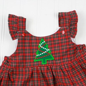 K&ouml;nnte beinhalten: Rotes und gr&uuml;nes Karo-Overallkleid mit einem gr&uuml;nen Weihnachtsbaum-Applikation. Der Baum hat wei&szlig;e Lichter und rote Kugeln.