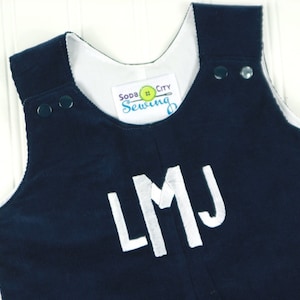 Puede incluir: Pantalón vaquero de pana azul marino con letras de fieltro blanco que deletrean "LMJ" en la parte delantera. El pantalón tiene tirantes blancos y una etiqueta blanca que dice "Soda City Sewing".