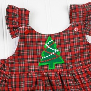 K&ouml;nnte beinhalten: Rotes und gr&uuml;nes Karo-Overallkleid mit einem gr&uuml;nen Filz-Weihnachtsbaum-Applikation. Der Baum hat wei&szlig;e und rote Perlen und einen roten Stern oben drauf.