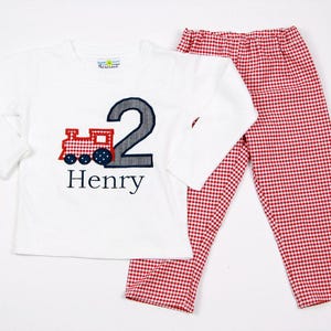 May include: White long-sleeve shirt with a red and blue train and the number 2 embroidered on it. The shirt also has the name "Henry" embroidered on it. Red and white gingham pants.