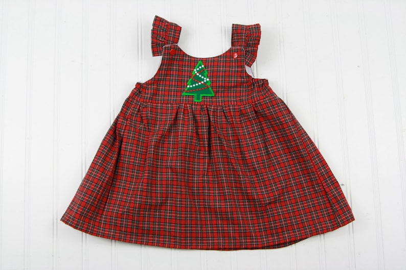 K&ouml;nnte beinhalten: Ein rotes und schwarzes kariertes, &auml;rmelloses Kleid mit einem gr&uuml;nen gestickten Weihnachtsbaum auf der Vorderseite.