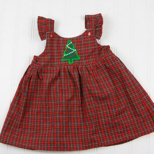 K&ouml;nnte beinhalten: Ein rotes und schwarzes kariertes, &auml;rmelloses Kleid mit einem gr&uuml;nen Weihnachtsbaum-Applikationen. Der Baum hat wei&szlig;e Lichter und einen roten Stern oben drauf.