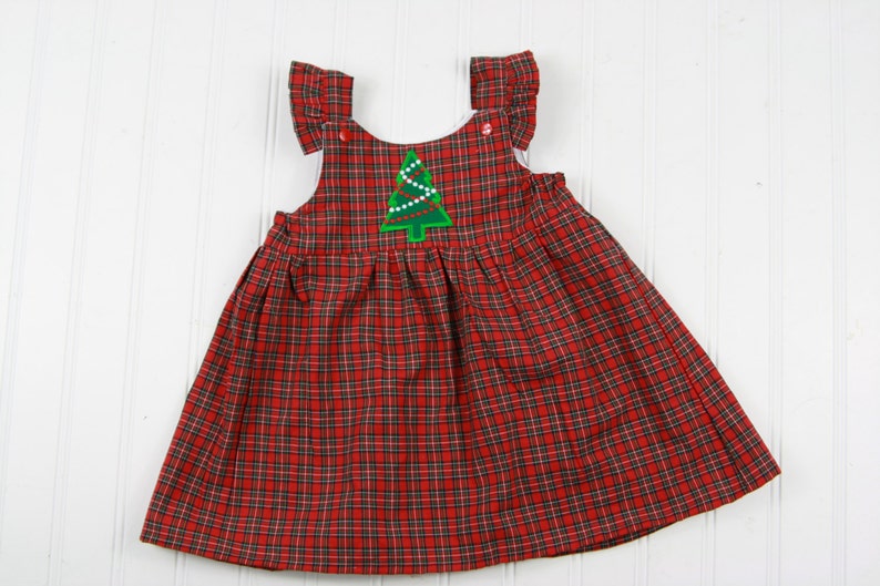 K&ouml;nnte beinhalten: Ein rotes und schwarzes kariertes, &auml;rmelloses Kleid mit einem gr&uuml;nen Weihnachtsbaum-Applikationen. Der Baum hat wei&szlig;e Lichter und einen roten Stern oben drauf.