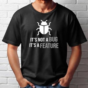 Może przedstawiać: Czarny t-shirt z krótkim rękawem z białą grafiką przedstawiającą ikonę chrząszcza nad napisem IT'S NOT A BUG IT'S A FEATURE wydrukowanym białymi wielkimi literami. Koszulka ma okrągły dekolt i standardowy krój.