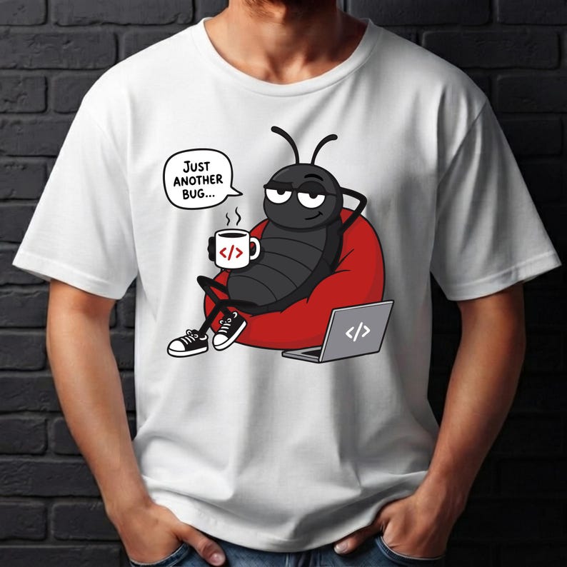 May include: A white short-sleeved t-shirt featuring a graphic of a black cartoon bug sitting in a red beanbag chair. The bug holds a white mug with code brackets and has a speech bubble that says Just Another Bug. A laptop with code brackets is nearby.