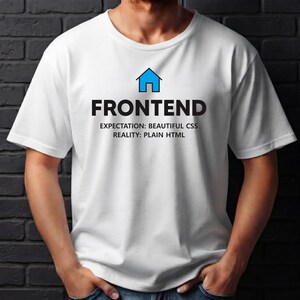以下が含まれることがあります： 白い半袖Tシャツで、青い家のアイコンの下に黒い文字でFRONTENDと書かれています。その下には、EXPECTATION: BEAUTIFUL CSS、REALITY: PLAIN HTMLという黒いテキストが配置されており、すべて衣服の前面中央にプリントされています。