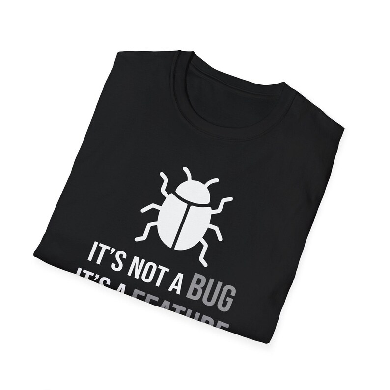 Może przedstawiać: Czarny t-shirt z białą grafiką przedstawiającą ikonę chrząszcza nad białym napisem IT'S NOT A BUG IT'S A FEATURE. Koszulka ma okrągły dekolt i kr&oacute;tkie rękawy, zaprezentowana w złożonej, płaskiej orientacji.