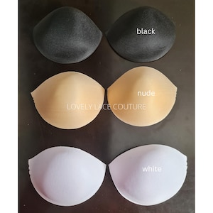 May include: Three pairs of moulded bra cups in black, nude, and white, arranged in rows. The text "black," "nude," and "white" labels each pair, while "LOVELY LACE COUTURE" is printed in the centre of the image between the cup sets.