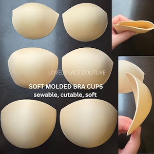May include: A set of beige, soft moulded bra cups with a smooth finish. The image includes the text LOVELY LACE COUTURE, SOFT MOLDED BRA CUPS, sewable, cutable, soft. These foam inserts are rounded and designed for garment construction.
