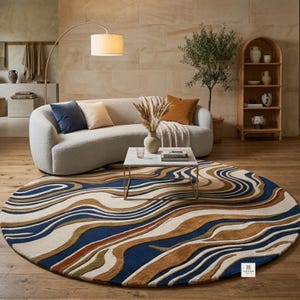 May include: A large round area rug featuring a wavy, abstract pattern in shades of deep blue, cream, tan, and brown. The rug has a textured, multi-level pile and includes a small white rectangular tag with the text KEYAN NEW YORK in the corner.