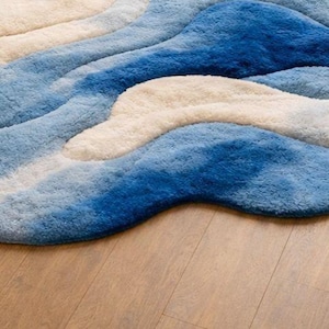 May include: A plush area rug featuring an abstract, wavy pattern in shades of deep blue, light blue, and cream. The rug has a thick, textured pile with organic, flowing curves that create a layered effect across the surface of the floor covering.