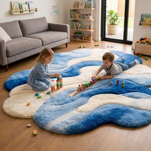 May include: A large, plush, cloud-shaped area rug featuring a wavy, ombre pattern in shades of blue and cream. The rug has a soft, textured surface and is laid out on a wooden floor, providing a comfortable space for play and floor-based activities.