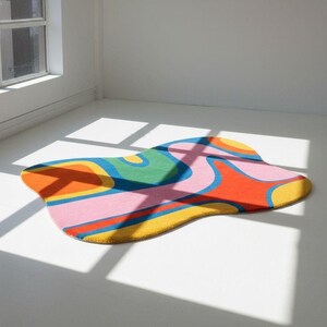 May include: An irregularly shaped area rug featuring a vibrant, multi-colored abstract pattern with flowing, organic curves. The design incorporates bold blocks of orange, bright yellow, light pink, deep green, and blue in a continuous, wavy layout.