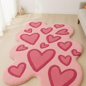 May include: An irregularly shaped, light pink area rug featuring a tufted texture. The rug is decorated with multiple dark pink heart-shaped motifs of varying sizes scattered across the surface, creating a repeating pattern throughout the piece.