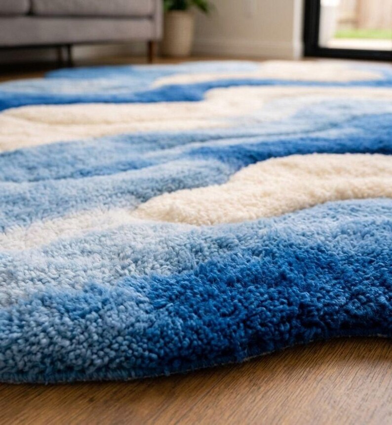 May include: A plush area rug featuring a wavy, abstract pattern in shades of deep blue, light blue, and cream. The rug has a thick, tufted texture with high-pile sections that create a dimensional, rippled effect across the entire surface area.