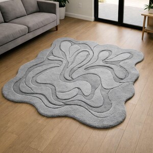 May include: An irregular, cloud-shaped area rug in a solid light gray color. The rug features a tufted, raised texture that creates a series of flowing, organic, wave-like patterns across its surface, adding depth and dimension to the floor covering.