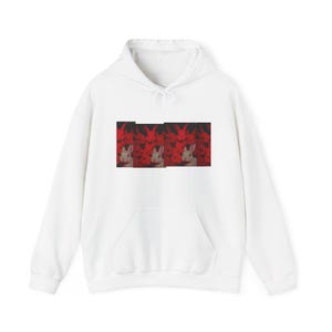 Puede incluir: Una sudadera con capucha blanca de manga larga que presenta un estampado gráfico rectangular central. El diseño muestra un patrón repetitivo de siluetas de conejos rojos sobre un fondo oscuro, con un conejo blanco en primer plano.