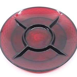 May include: A round, divided serving dish in a deep red hue. The dish features a central circular compartment and four pie-shaped sections, separated by black dividers. The surface has a textured, diamond-like pattern.
