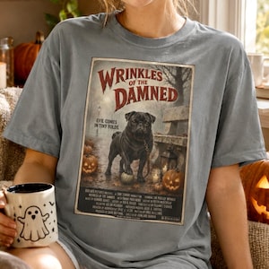 Może przedstawiać: Szary t-shirt z nadrukiem czarnego mopsa stojącego na ścieżce z dyniami i kamienną ławką. Tekst głosi Wrinkles of the Damned, Evil Comes in Tiny Folds i zawiera napisy w stylu filmowym. Trzymany jest biały kubek z nadrukiem ducha.