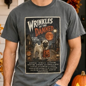 Könnte beinhalten: Ein anthrazitfarbenes T-Shirt mit einem Grafikdruck eines Mopses, der eine Kürbistasche hält. Das Design ähnelt einem alten Horrorfilmplakat mit dem Titel Wrinkles of the Damned, einem Vollmond, einer Straßenlaterne und dem Text Evil Comes in Tiny Folds.