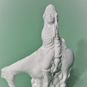 May include: White ceramic figurine of a Native American person riding a horse. The figurine is detailed with feathers and a headdress.