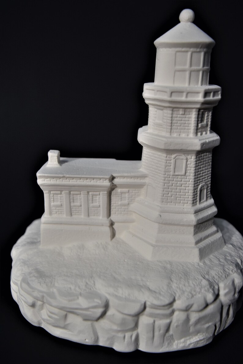 May include: White ceramic lighthouse figurine with a detailed brick exterior and a small chimney on the roof. The lighthouse is perched on a rocky base.
