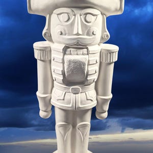 May include: A white ceramic nutcracker figurine with a tall hat and a detailed face. The nutcracker is standing on a round base.