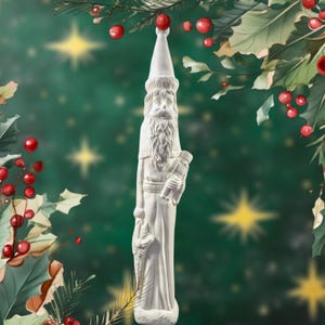 May include: White ceramic Christmas ornament shaped like a Santa Claus holding a nutcracker. The ornament has a detailed face and beard, and is wearing a long robe.
