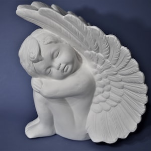 May include: White ceramic angel figurine with wings, sleeping with its head resting on its arm. The angel is in a sitting position.