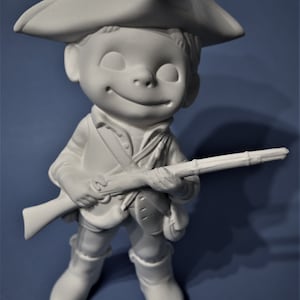 May include: A white ceramic figurine of a smiling boy in a tricorn hat, holding a rifle. The figure is dressed in a colonial-style outfit, including a jacket, boots, and a shoulder strap. The figurine is on a blue background.