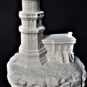 May include: White ceramic lighthouse figurine with a brick-like texture. The lighthouse has a small house attached to it and sits on a rocky base. The base is inscribed with "Split Rock, Minn."