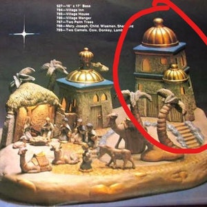 May include: A ceramic nativity scene with a stable, palm trees, and a three-story building with a gold roof. The scene is lit with small lights. 527-16 17 Base 704-Village Inn 765-Village House 786-Village Manger 787-Two Palm Trees 788-Mary. Joseph, Child. Wisemen. She d 753-Two Camels, Cow, Donkey. Lamb