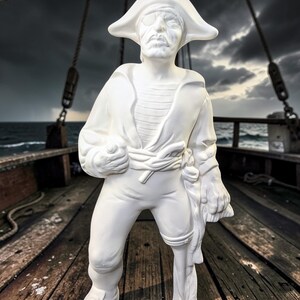 May include: A white pirate statue with a tricorn hat, eye patch, and a stern expression. The figure is dressed in a long coat, striped shirt, and breeches, holding a rolled cloth. The statue stands on a wooden deck with a stormy sea backdrop.